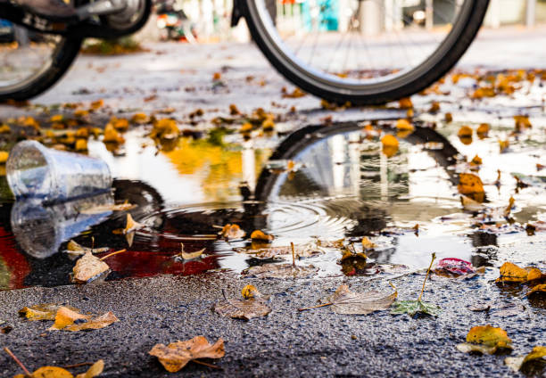 charco con hojas otoñales de colores y reflejos en el que pasa una bicicleta - regenwetter fotografías e imágenes de stock
