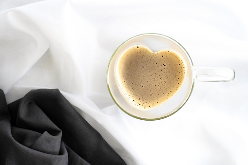 Heart-shaped glass cup filled with coffee on white satin fabric, gray fabric with pictured, top view, horizontal