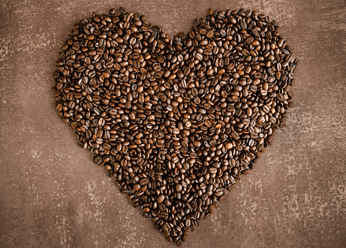Heart made of roasted coffee beans on a light brown mottled background, horizontal