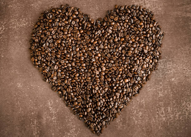 roasted coffee beans heartshaped Heart made of roasted coffee beans on a light brown mottled background, horizontal tasse café stock pictures, royalty-free photos & images