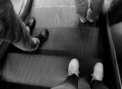 Feet of three people on an escalator, view from above, horizontal