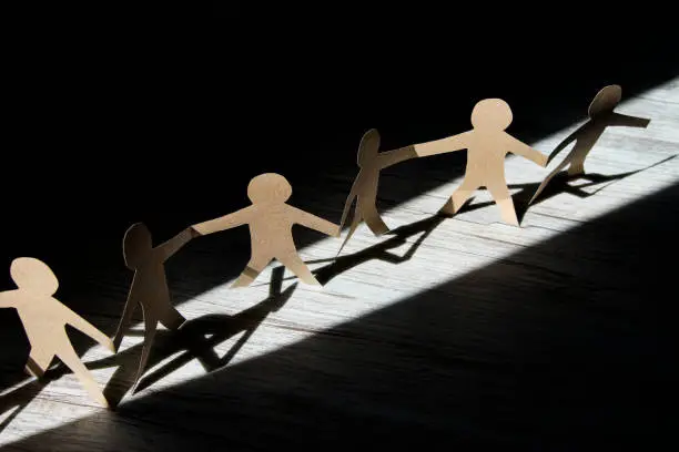 Paper cut paper human chain made of brown cardboard in cone of light, black background, horizontal
