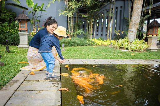 Pretty mother and a young baby relax on a rock while watching the Koi fish swim by