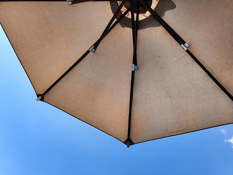 Low angle view of an opened beach fabric umbrella against the blue sunny sky, view from under parasol, holiday or vacation concept, with copy space