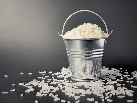 White rice in miniature bucket with gray background. Stock photo.