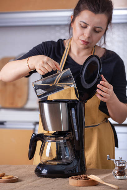 istock Woman adding water to the coffee machine and preparing coffee in the kitchen. 1984500202