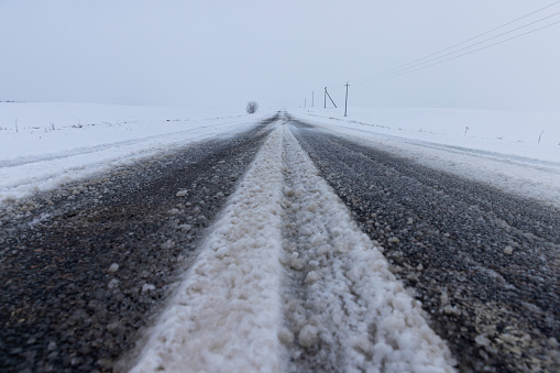 a snow-covered paved road in the winter season in a snowfall, a road during a snowfall, spots from falling snowflakes are visible in the sky