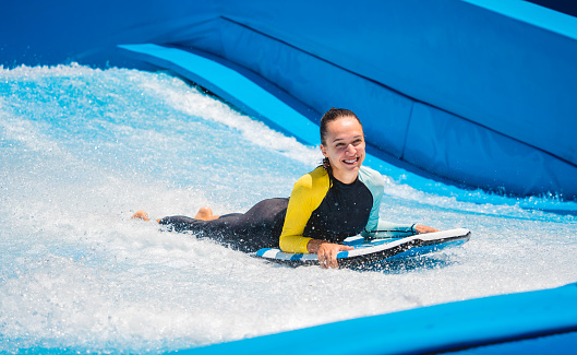 Beautiful young woman surfing on a wave simulator at a water amusement park.