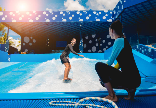 istock Young man surfing with trainer on a wave simulator at a water amusement park 1984537461