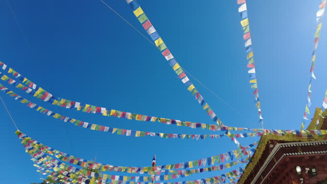 Tilt down from blue sky and colorful flags to Soma Gompa building.