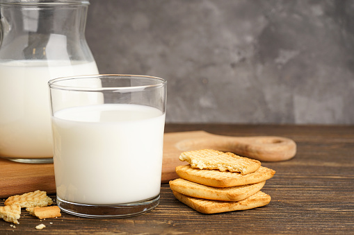 Milk in glass and jug with cookie on wooden table on a grey background. Close-up.