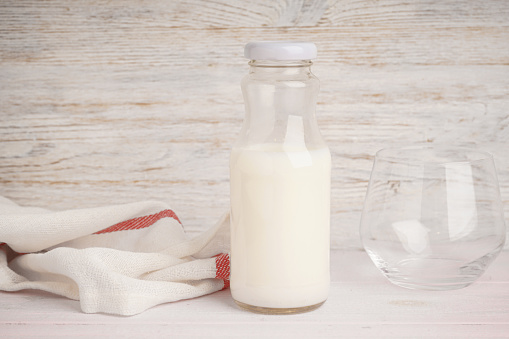 Milk in jar and glass on the light wooden background.