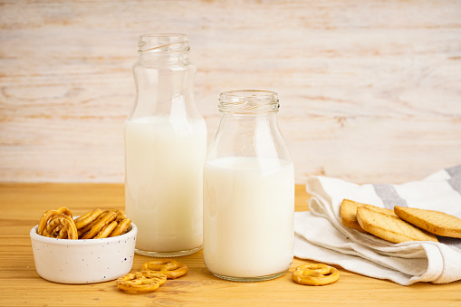 Milk in glass and jug with cookie on wooden table and light background. Close-up.