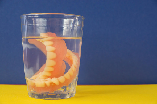Glass glass with water and dentures on a yellow background with a blue wall