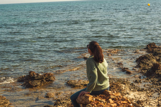 istock Brunette Sitting On A Rock On The Beach 1984638678