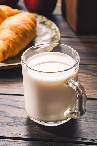 Glass mug with milk with a croissant on wooden table