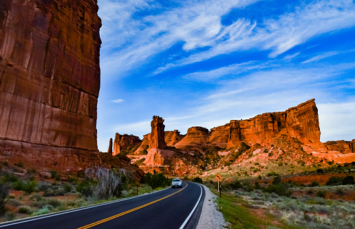Wide open American road goes off into the horizon featuring jagged mesa formations of Monument Valley 