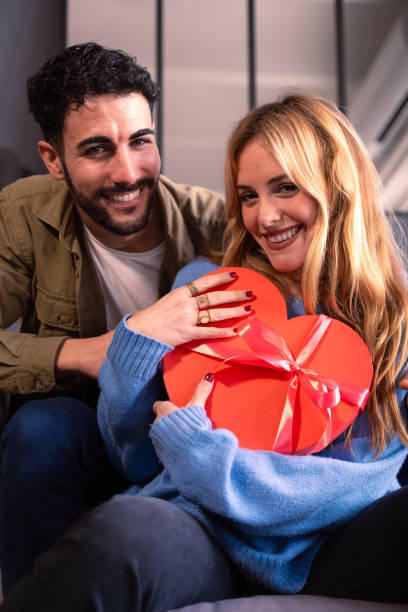 istock Vertical shot Smiling young couple with a heart-shaped gift box looking at camera.Lovers 1984698632