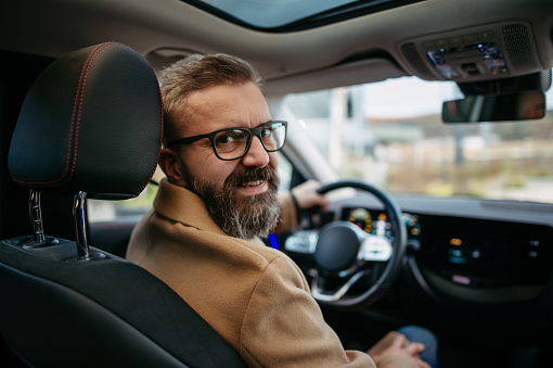 Portrait of mature handsome man sitting in electric car, looking back over the shoulder.