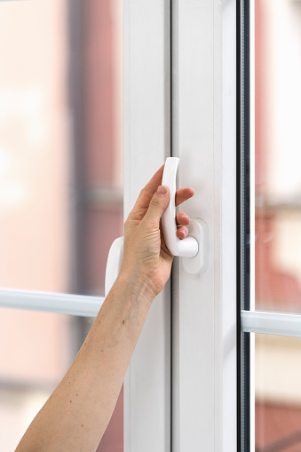 Vertical shot of woman hand holding handle, turning up and opening new modern white balcony door or pvc window at home. Household concepts, close up view