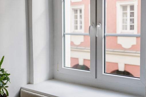 Close up of empty windowsill and plastic windows with white frames overlooking view on building in living room at apartment. Home interior. Copy space