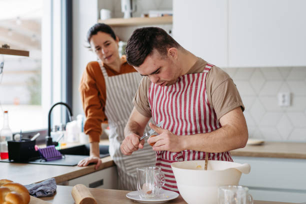 istock Young man with Down syndrome preparing breakfast with his mother at home, cracking eggs. Morning routine for man with Down syndrome. 1984740694