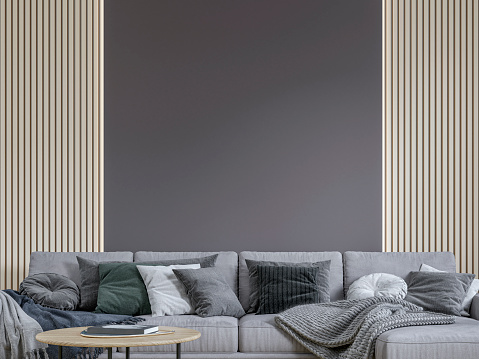 Front view of a cozy, elegant, and modern living room with a gray textile sofa, low coffee table, and decorations (multicolored pillows, blankets, a golden tray, books) in front of a half plaster brown wall, half natural wood paneled wall with copy space. A slight vintage effect was added. 3D rendered image.