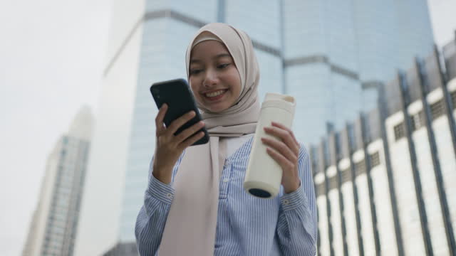 Young Asian Muslim woman using Mobile Phone searching internet in outdoor work place
