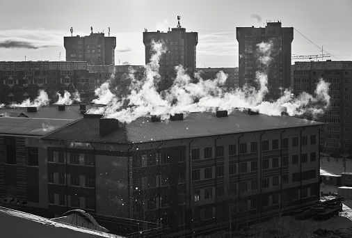 Cityscape of residential district, a smoke and steam are rising up from the pipes on the housetop at a sunny frosty day, black and white image
