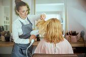pensive woman hair salon worker blowout hair with hair dryer