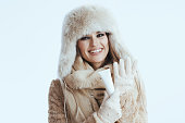 happy stylish woman in winter coat and fur hat on white
