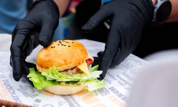 istock Hambuger mini, Professional  Hand chef holding fresh delicious and tasty handmade burger, garnished with salad, tomatoes, and cucumber in a close-up shot, Fast food for your quick lifestyle 1984894774