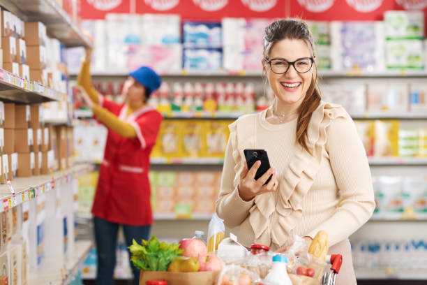 istock Smiling woman using a smartphone at the grocery store 1984906904