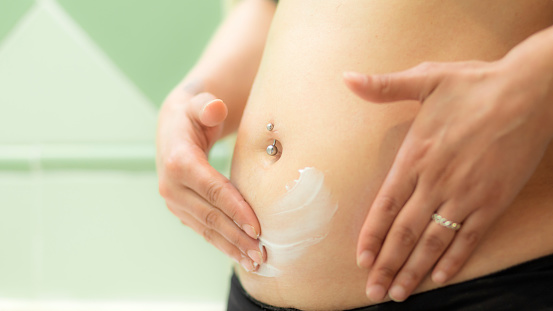 Pregnant woman putting anti-stretch mark cream on her belly to keep her skin hydrated and prevent scars. Woman using cream in the first months of pregnancy to prevent stretch marks during motherhood