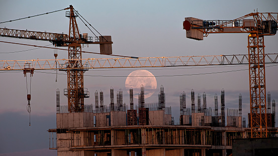 Full moon is going to set over the under construction residential complex.