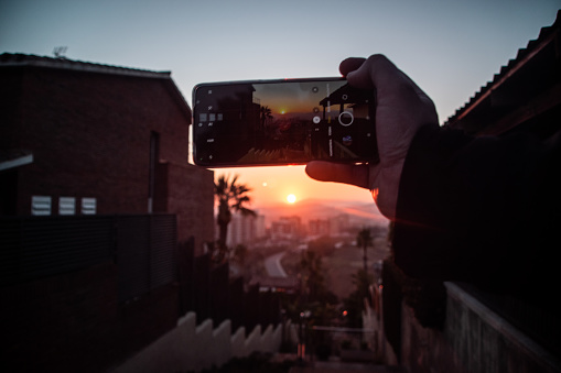 image of a phone taking a photograph of a sunset between buildings