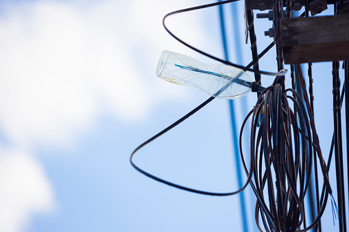 A plastic bottle protects the ends of exposed electrical wires from water outdoors. Roll of wires with plastic bottle against blue sky