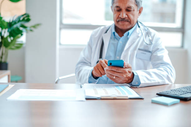 istock Senior male physician texting on cellphone at work desk 1985061188