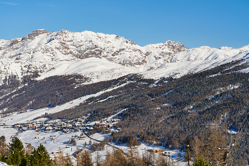 Panoramic view of scenic white winter wonderland mountain scenery in the Alps with traditional wooden mountain chalets on a cold sunny day with blue sky and clouds
