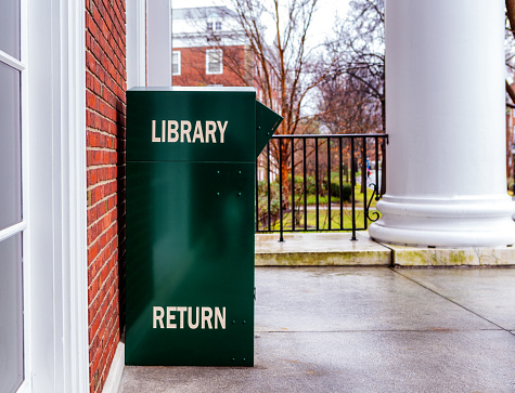 Boston, Massachusetts, USA - January 30, 2024: A green library book return box against the wall of the Baker Library on the Harvard Business School (HBS) campus. Dedicated in 1927 and named for George F. Baker, the benefactor who funded HBS's original campus. It is the largest business library in the world. Selective focus.