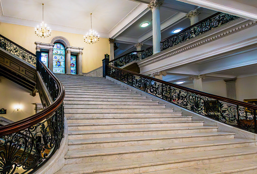 Boston, Massachusetts, USA - February 1, 2024: View up the Grand Staircase (aka Main Staircase) of the Massachusetts State House. Near the top of the staircase is a stained glass window showing the evolution of the Commonwealth of Massachusetts' state seal.