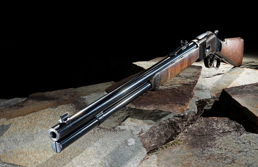 Repeating lever action rifle like the kind used in the wild west on stones that show off the oiled wood stock and deep bluing on the metalwork.