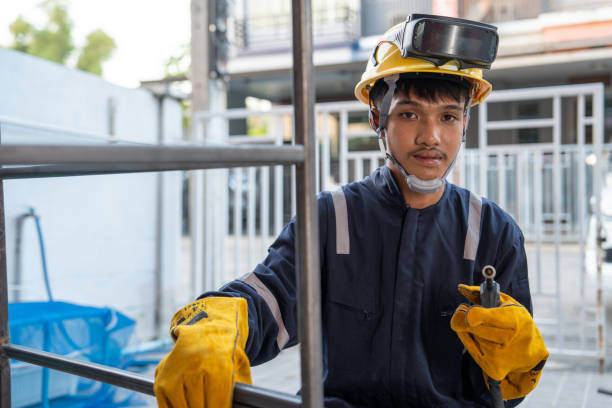 Asian worker wearing safety suit uses MIG welding machine.