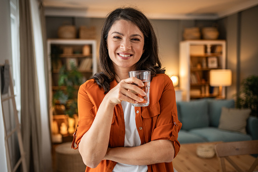 Portrait of a smiling woman holding a glass of fresh clean drinking water. Concept of healthy lifestyle and fluid intake