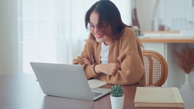 Happy positive young asian woman enjoying online communication at home, Female using wifi while video conferencing with friend, sitting in front of open laptop