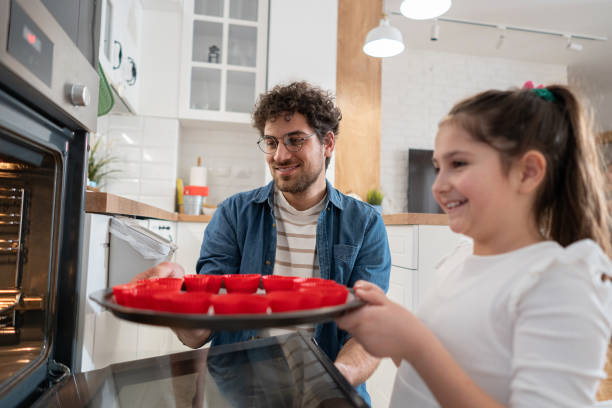 istock Daughter with father put an muffin mixture into oven, to bake 1985187819