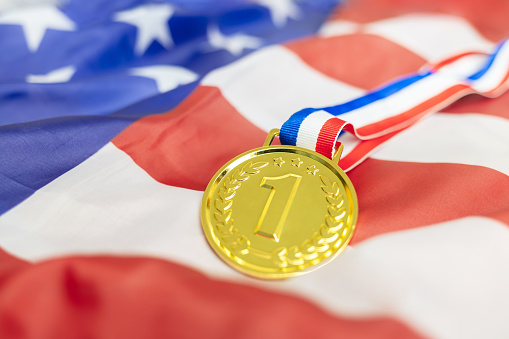 A radiant gold medal proudly rests upon the American flag, symbolizing national pride and fervent support for American athletes in global sporting events