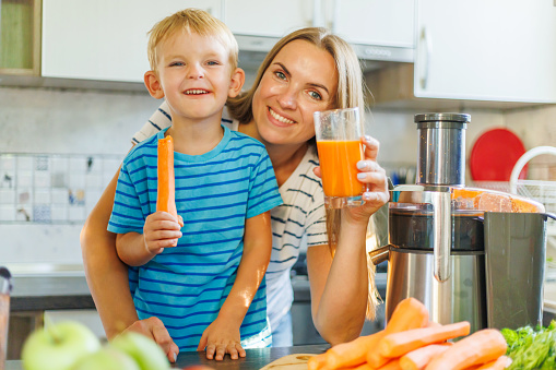 Smiling woman and child with carrot juice in a sunny kitchen
