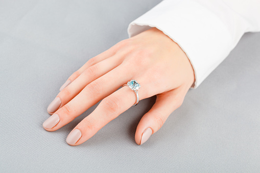 Beautiful female hand with gold ring with diamonds and aquamarine on gray background close-up