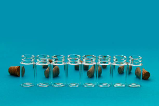 Glass bottles arranged in a row with corks behind that can be seen through the glass